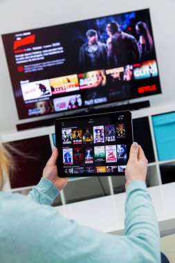 Woman Holding a touch pad and switching channels on France Netflix HomePage. with TV set on background. clipart