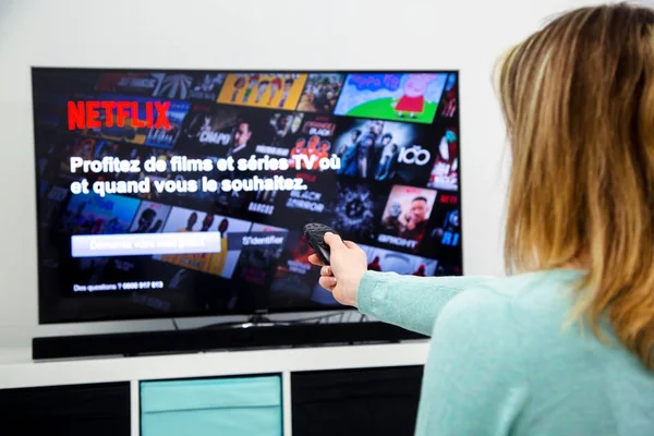 Bir Tv uzaktan kumanda Holding ve Fransa Netflix ana sayfasında kanallar anahtarlama kadın — Stok fotoğraf
