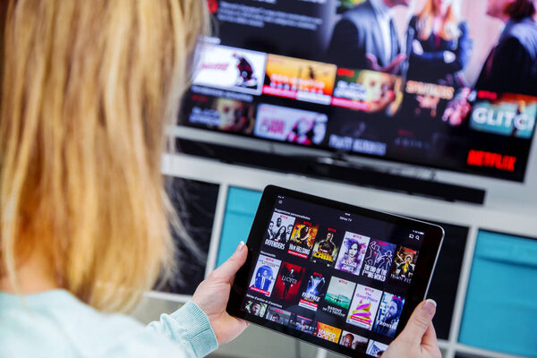 Woman Holding a touch pad and switching channels on France Netflix HomePage. with TV set on background.