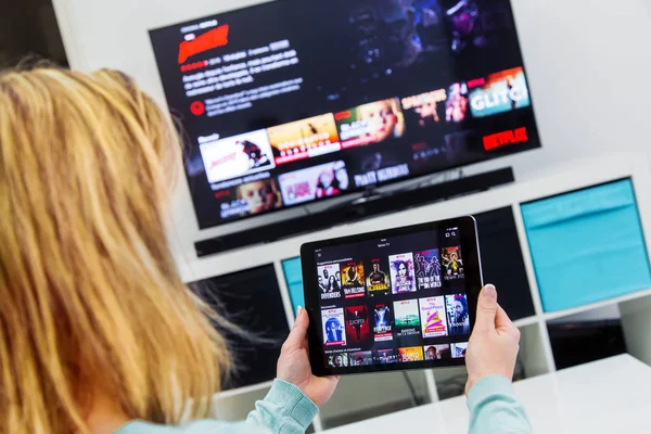Mujer Sosteniendo un panel táctil y cambiando canales en Francia Netflix HomePage. con televisor en el fondo . —  Fotos de Stock
