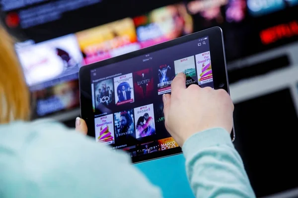 Mujer Sosteniendo un panel táctil y cambiando canales en Francia Netflix HomePage. con televisor en el fondo . Imagen de stock