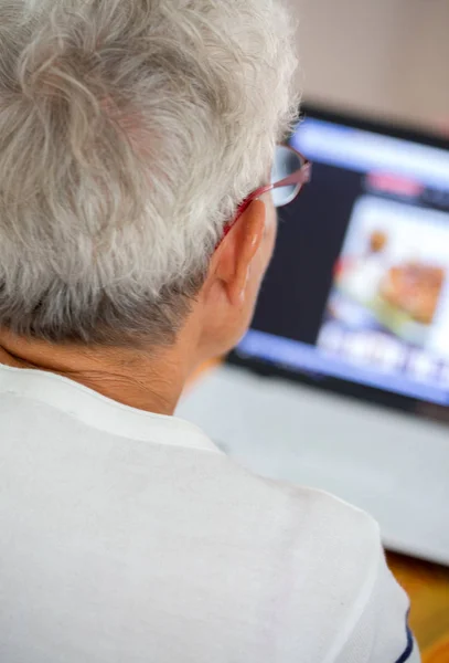 Old person in glasses busy working with a laptop — Stock Photo, Image