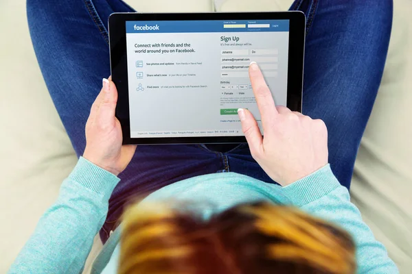 Woman sitting on her couch using touch pad to create a new user account on facebook — Stock Photo, Image