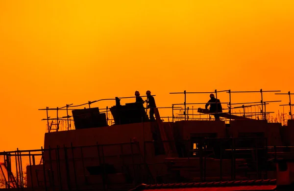 Trabajadores de la construcción que trabajan en un edificio bajo una puesta de sol —  Fotos de Stock