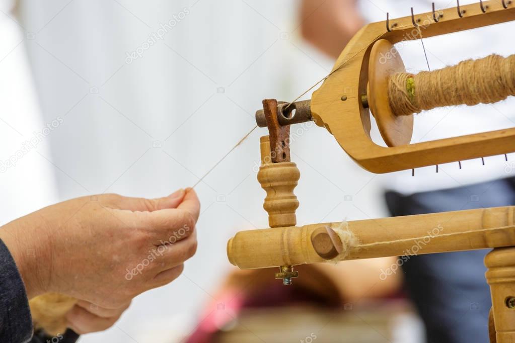 old woman using an old wool spinning wheel