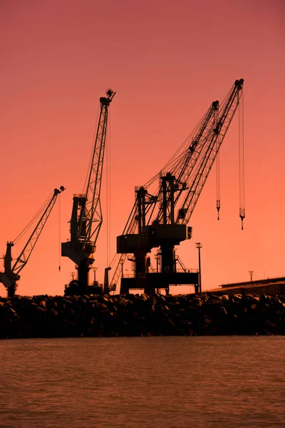 Astillero grúas siluetas contra una hermosa puesta de sol naranja . — Foto de Stock