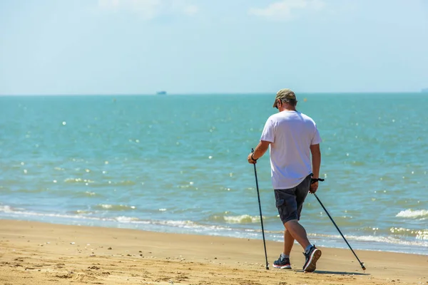 Active senior man walking with nordic walking poles on the beach — Stock Photo, Image