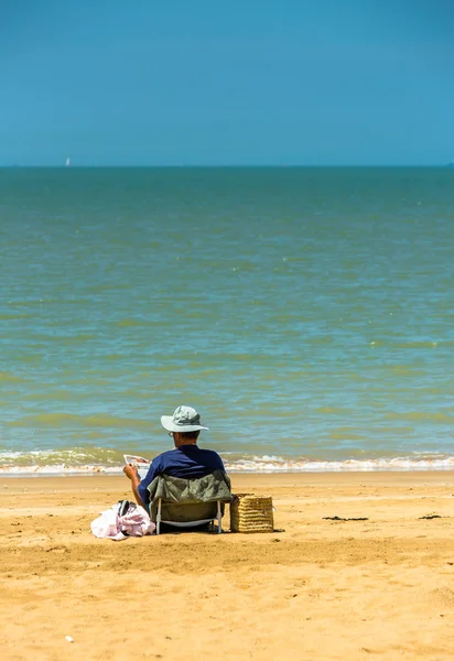 Senior man läsa en tidning på stranden vid vattnet. — Stockfoto