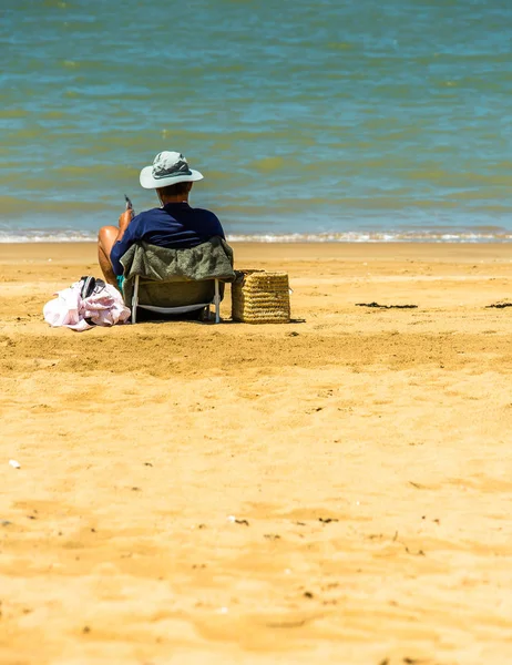 Ανώτερος άνθρωπος διαβάζει μια εφημερίδα στην παραλία στην άκρη του νερού. — Φωτογραφία Αρχείου