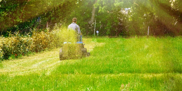 Vue arrière d'un homme assis sur son tracteur tondant sa pelouse par temps ensoleillé — Photo