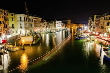 Rialto Köprüsü 'ndeki suya yansıyan nehir mekiklerinin parlak izleri.