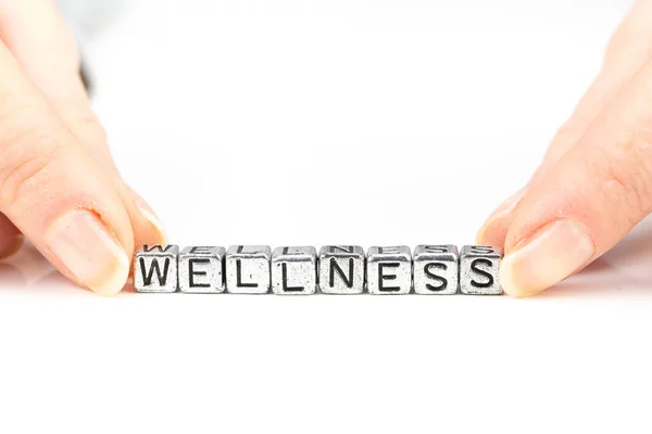 Wellness concept with cube letters and a woman's hand surrounding the word — Stock Photo, Image