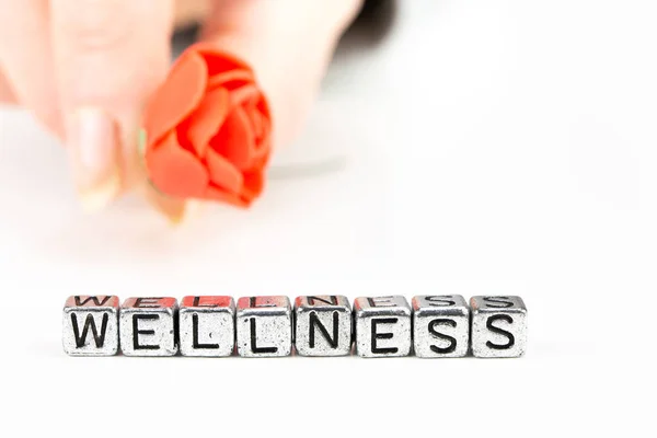 Wellness concept met kubus letters en een vrouw hand met een roos — Stockfoto