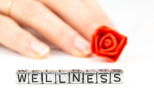 Wellness concept met kubus letters en een vrouw hand met een roos — Stockfoto