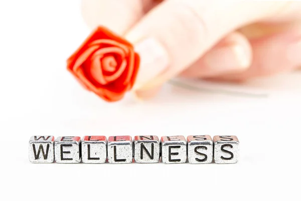 Wellness concept with cube letters and a woman hand holding a rose — Stock Photo, Image