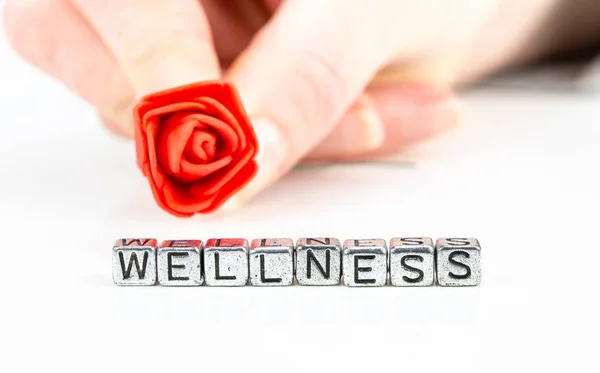 Wellness concept with cube letters and a woman hand holding a rose — Stock Photo, Image