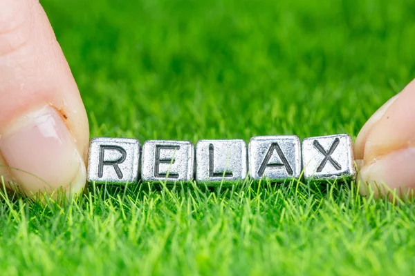 Word Relax geschreven in metalen letters op gras gelegd en tussen de vingers van een vrouw gehouden. Concept van wellness achtergrond — Stockfoto