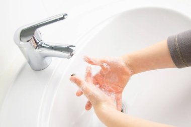 Çocuk tuvalette sabunla ellerini temizliyor ve yıkıyor.