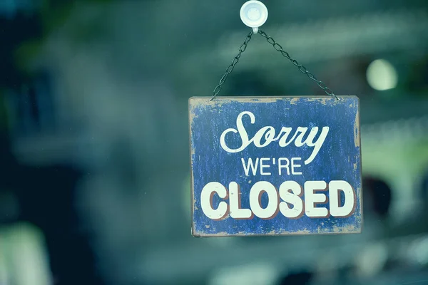 Close-up on a blue closed sign in the window of a shop displaying the message \