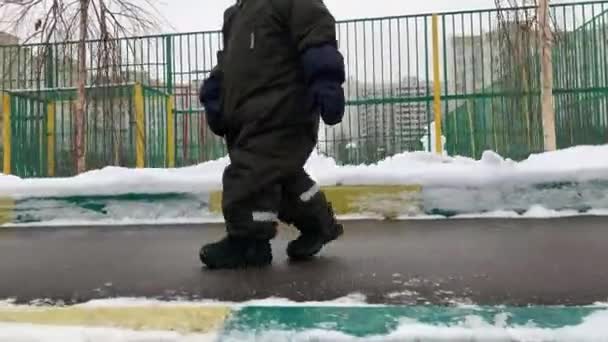 Voeten van een klein kind nemen mijn eerste stappen op straat in de winter sneeuw en asfalt. Kleine baby leert lopen. Eerste stappen. 60 fps, 4k. Sluit je voeten. Gelukkige jeugd. Gezin. — Stockvideo