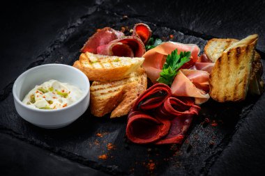 Etli şarküteri tabağı siyah desenli bir arka planda sıralanmış.