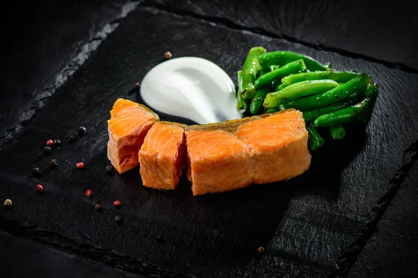 Fried trout with beans on a black textured background — Stock Photo, Image