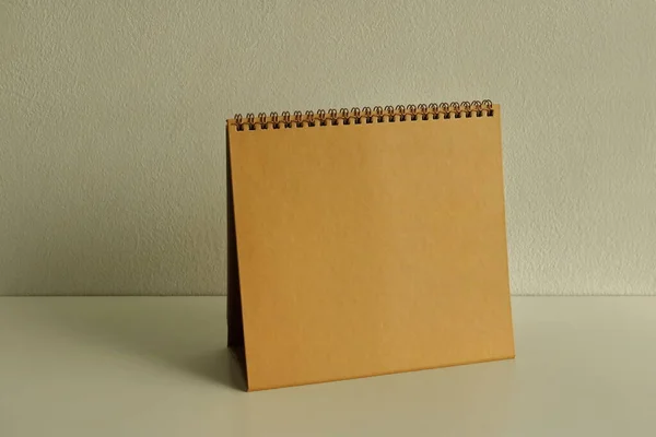 Empty golden spiral binding desk calendar placed on white wooden table with sunlight and shadow