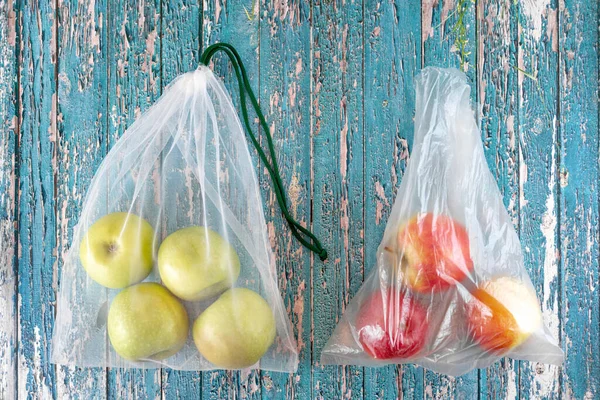 eco bag with apples and traditional plastic disposable plastic bag with apples.Concept of eco-friendly materials. Close up. Copy space. light wood background