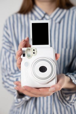 Kızın elinde fotoğraf çerçeveleri ve beyaz bir kamera var. Modern polaroid fotoğraf makinesi, beyaz tahta arka plan. Üst manzara, yumuşak minimum düz konum kompozisyonu. moda blogcusu, güzellik teknolojisi