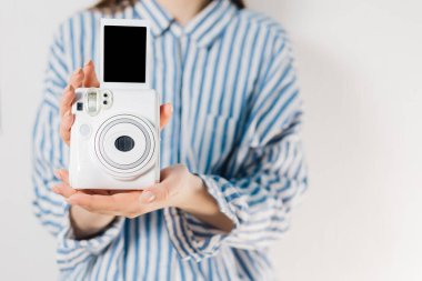 Kızın elinde fotoğraf çerçeveleri ve beyaz bir kamera var. Modern polaroid fotoğraf makinesi, beyaz tahta arka plan. Üst manzara, yumuşak minimum düz konum kompozisyonu. moda blogcusu, güzellik teknolojisi