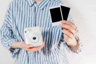 Kızın elinde fotoğraf çerçeveleri ve beyaz bir kamera var. Modern polaroid fotoğraf makinesi, beyaz tahta arka plan. Üst manzara, yumuşak minimum düz konum kompozisyonu. moda blogcusu, güzellik teknolojisi