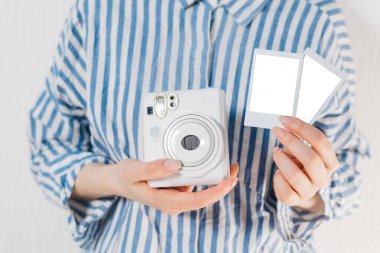 Kızın elinde fotoğraf çerçeveleri ve beyaz bir kamera var. Modern polaroid fotoğraf makinesi, beyaz tahta arka plan. Üst manzara, yumuşak minimum düz konum kompozisyonu. moda blogcusu, güzellik teknolojisi