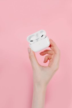 Hava kapsülleri uzmanı. Kablosuz şarj davasıyla. Pembe arka planda New Airpods profesyoneli. Hava kapsülü. Kadın kulaklıkları. Elinde kablosuz kulaklık var.
