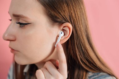 Beyaz kablosuz kulaklıklı pembe arka planda bir kız. Hava kapsülleri. Kablosuz şarj davasıyla. Pembe arka planda yeni hava araçları 2019. Hava podları. Kadın kulaklıkları. Boşluğu Kopyala