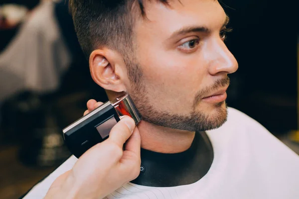 Portrait  man being trimmed with professional electric clipper machine in barbershop.Male beauty treatment concept. guy getting new haircut in barber salon.