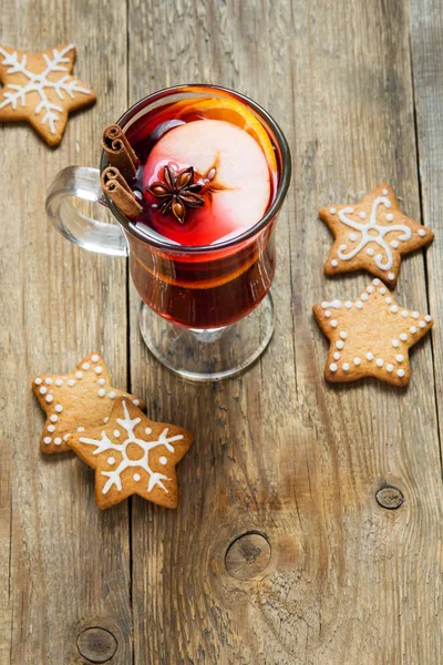 Christmas hot drink - mulled wine with fruits, cinnamon stick, star anise and festive Christmas gingerbread cookies over rustic wooden background with copy space, top view