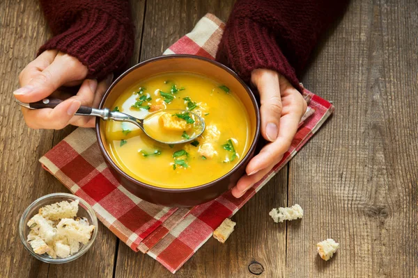 Woman hands holding bowl of vegetable soup with parsley and croutons over wooden background - healthy winter vegetarian food