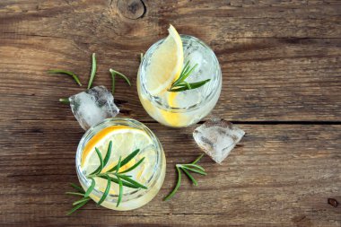 Limon, biberiye ve buz üzerinde rustik ahşap masa, kopya alanı ile alkollü içki (cin tonik kokteyl)