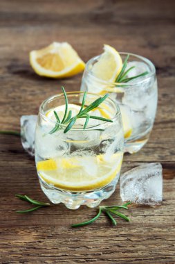 Limon, biberiye ve buz üzerinde rustik ahşap masa, kopya alanı ile alkollü içki (cin tonik kokteyl)