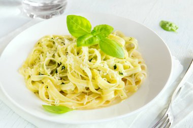Beyaz tabakta - sağlıklı ev yapımı makarna tagliatelle makarna pesto sos, peynir ve fesleğen yaprakları