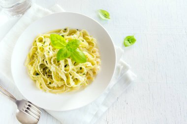 Beyaz tabakta - sağlıklı ev yapımı makarna tagliatelle makarna pesto sos, peynir ve fesleğen yaprakları