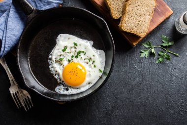 Yağda yumurta. Kızartma tavasındaki sahanda yumurtanın yakın görüntüsü. Demir tavada maydanozlu, tuzlu ve baharatlı yumurta ve siyah arka plan..