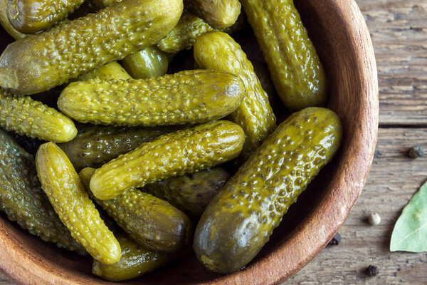 Pickles. Bowl of pickled gherkins (cucumbers) over rustic wooden background close up.