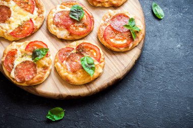 Mini Pizza - biber, peynir, domates ve fesleğen rustik siyah taş zemin üzerine taze ev yapımı mini pizza.