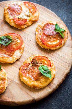 Mini Pizza - biber, peynir, domates ve fesleğen rustik siyah taş zemin üzerine taze ev yapımı mini pizza.