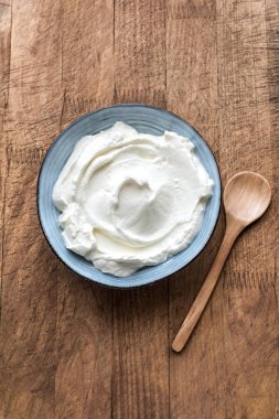 Ahşap arka planda seramik kasede doğal Yunan yoğurdu, üst manzara. Taze ev yapımı organik yoğurt veya ekşi krema..