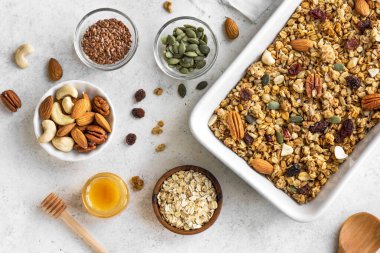 Homemade granola with nuts and seeds on baking sheet with ingredients. Granola for healthy breakfast on white, top view, flat lay. clipart