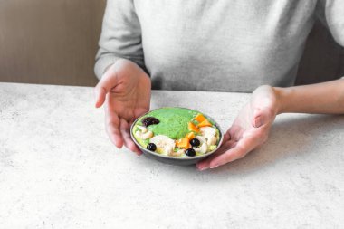 Sağlıklı kahvaltı kasesi yiyor. Yeşil smoothie, granola, fındık ve meyveler kadın ellerinde seramik kasede. Temiz yemek, diyet, detoks, vejetaryen, vejetaryen gıda konsepti