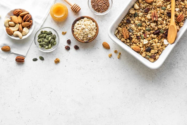 材料とベーキングシート上のナッツや種子を持つ自家製グラノーラ 白で健康的な朝食のためのグラノーラ トップビュー コピースペース — ストック写真