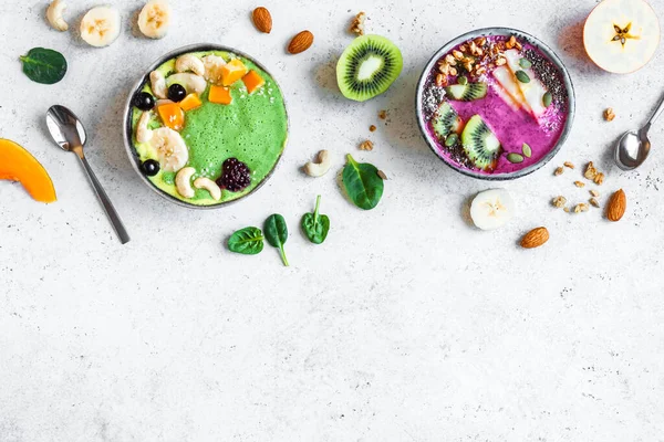 Colorful Smoothie Bowls for healthy detox breakfast, top view, copy space. Green spinach and berry smoothie bowls with various toppings. Vegan raw food, healthy eating concept.